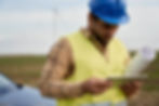 latin-male-engineer-holding-digital-tablet-standing-wind-turbine-field-with-paper-project.