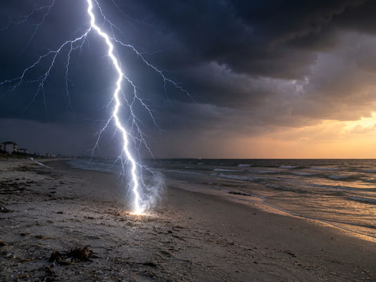 A lightning bolt strikes a sandy beach during a coastal thunderstorm, illustrating how lightning can turn silica-rich beach sand into natural glass called fulgurites.