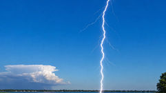 Lightning strikes from a clear blue sky while a distant thunderstorm sits on the horizon, illustrating the weather phenomenon known as a “bolt from the blue.”