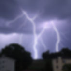 Intense lightning illuminates the night sky over suburban homes, highlighting the power of the storm against the dark clouds.