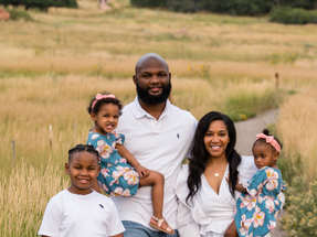 Mother and father smiling and holding two small girls and young son standing by their side in front of open field