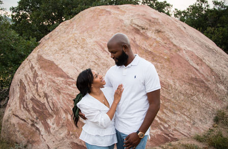 Couple in white tops and jean bottoms standing in front of a rock formation closeup.
