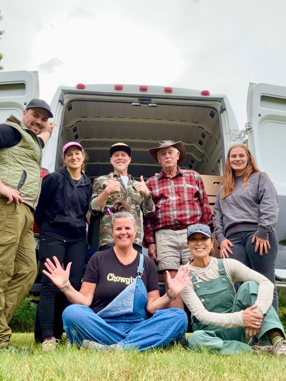 A group of Chowgirls team members participating in a partnership with a local produce farmer. The group is posing in front of a work van.