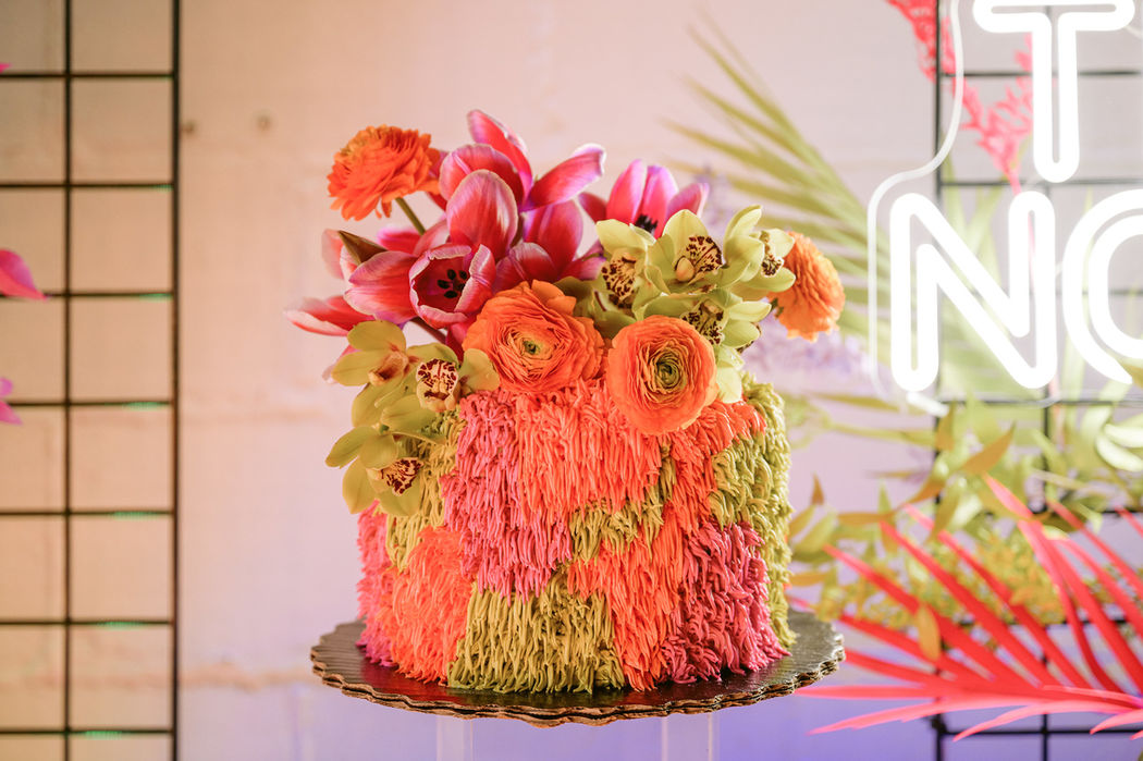 A fun quirky orange and yellow cake topped with pink, orange, and yellow flowers.