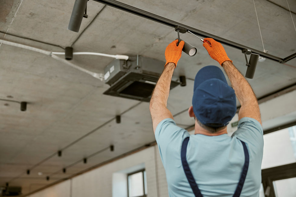 Worker in blue cap and gloves adjusts track lighting on a concrete ceiling indoors. Room appears industrial with calm atmosphere.
