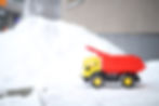 Pile of snow next to a toy yellow and red dump truck