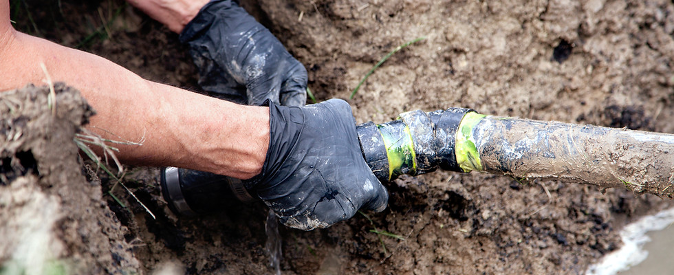 Spartan Plumber wearing gloves working on a broken sewer pipe