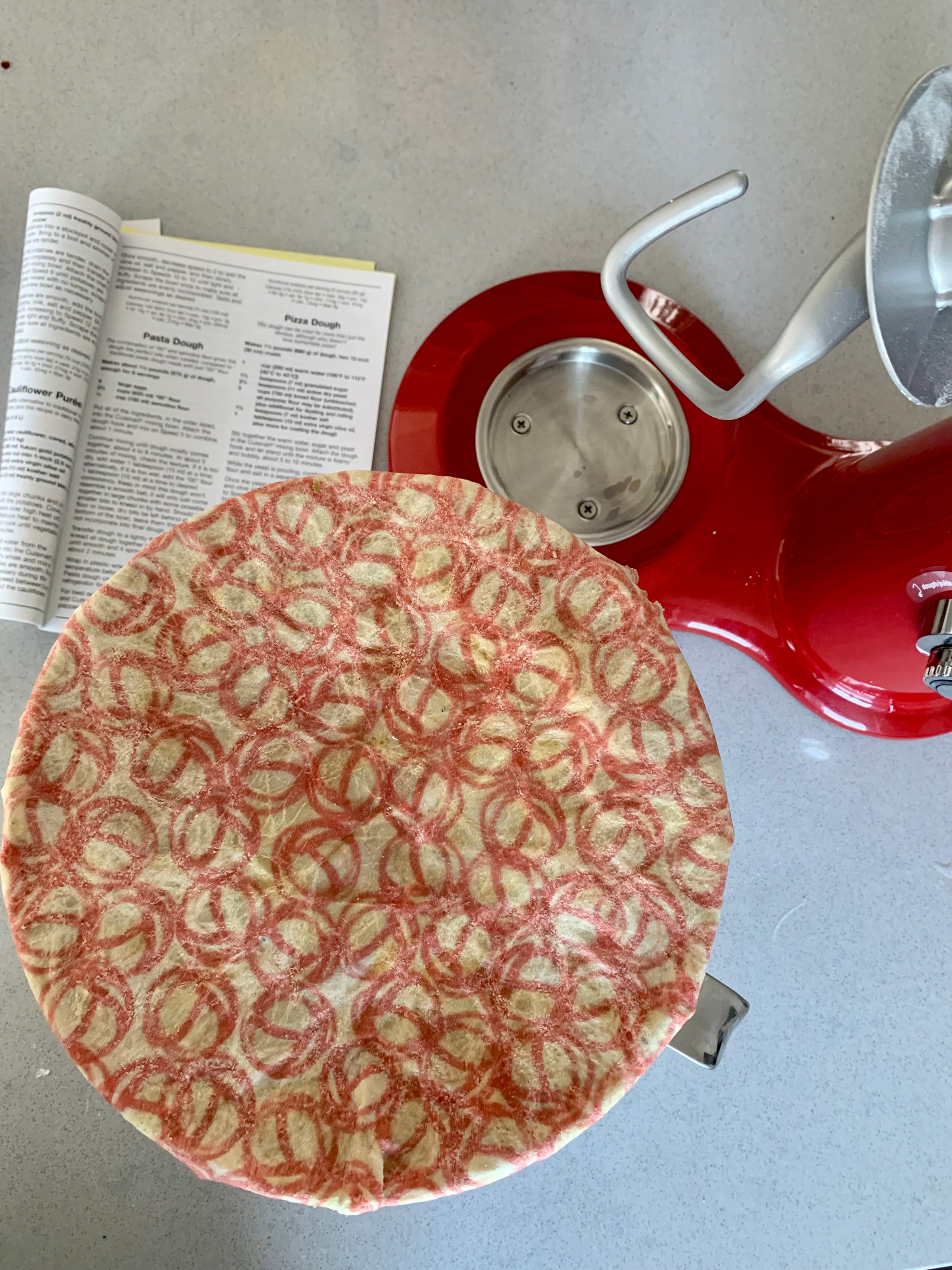 a white and pink beeswax wrap covers a bowl full of pizza dough so it can rise