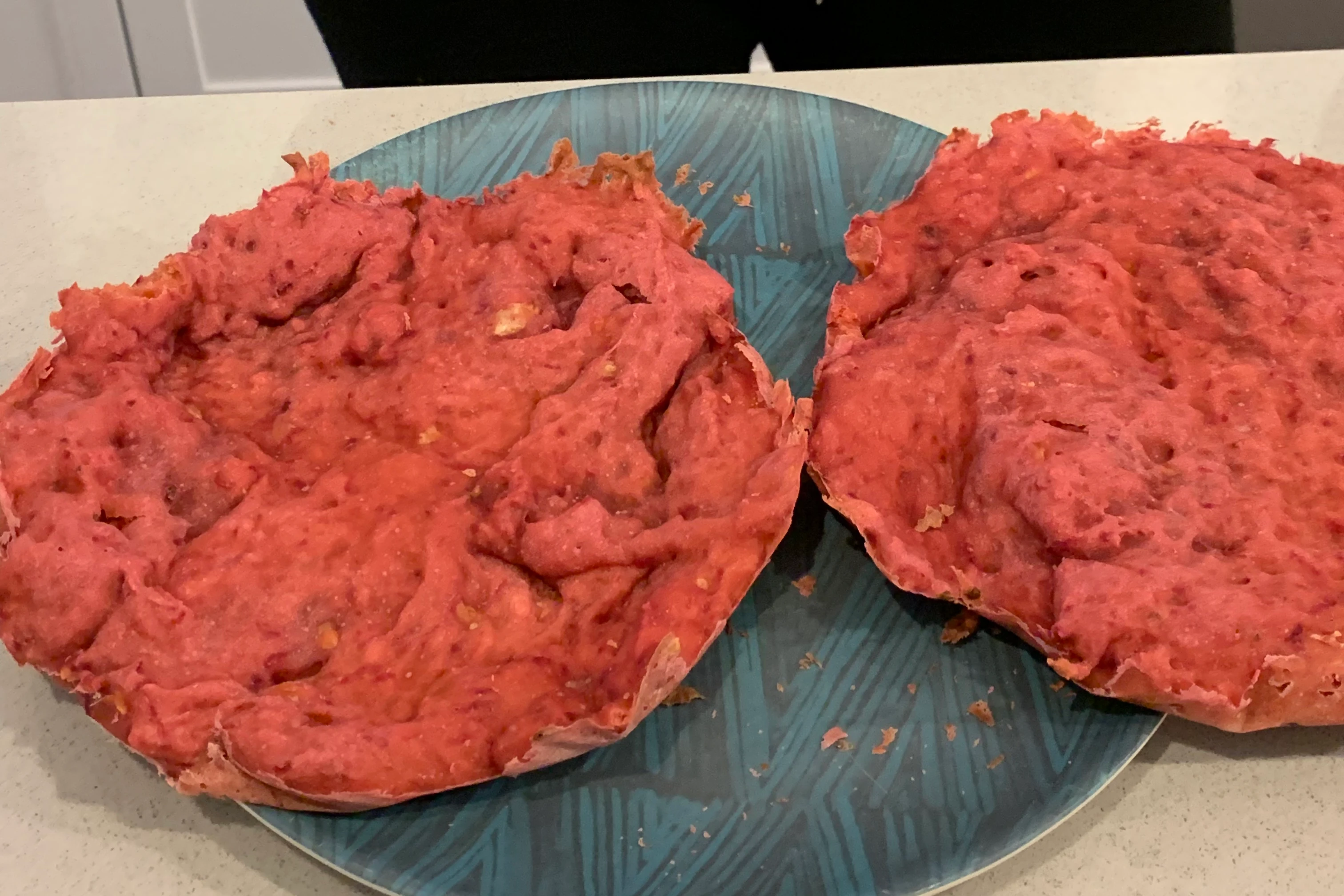 two round slabs of cake sit on a blue plate on a grey counter. the pieces of cake look like ground beef
