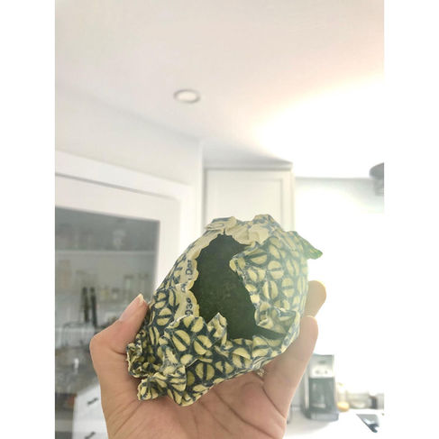 a hand holds up an avocado which is covered in a white and blue beeswax wrap