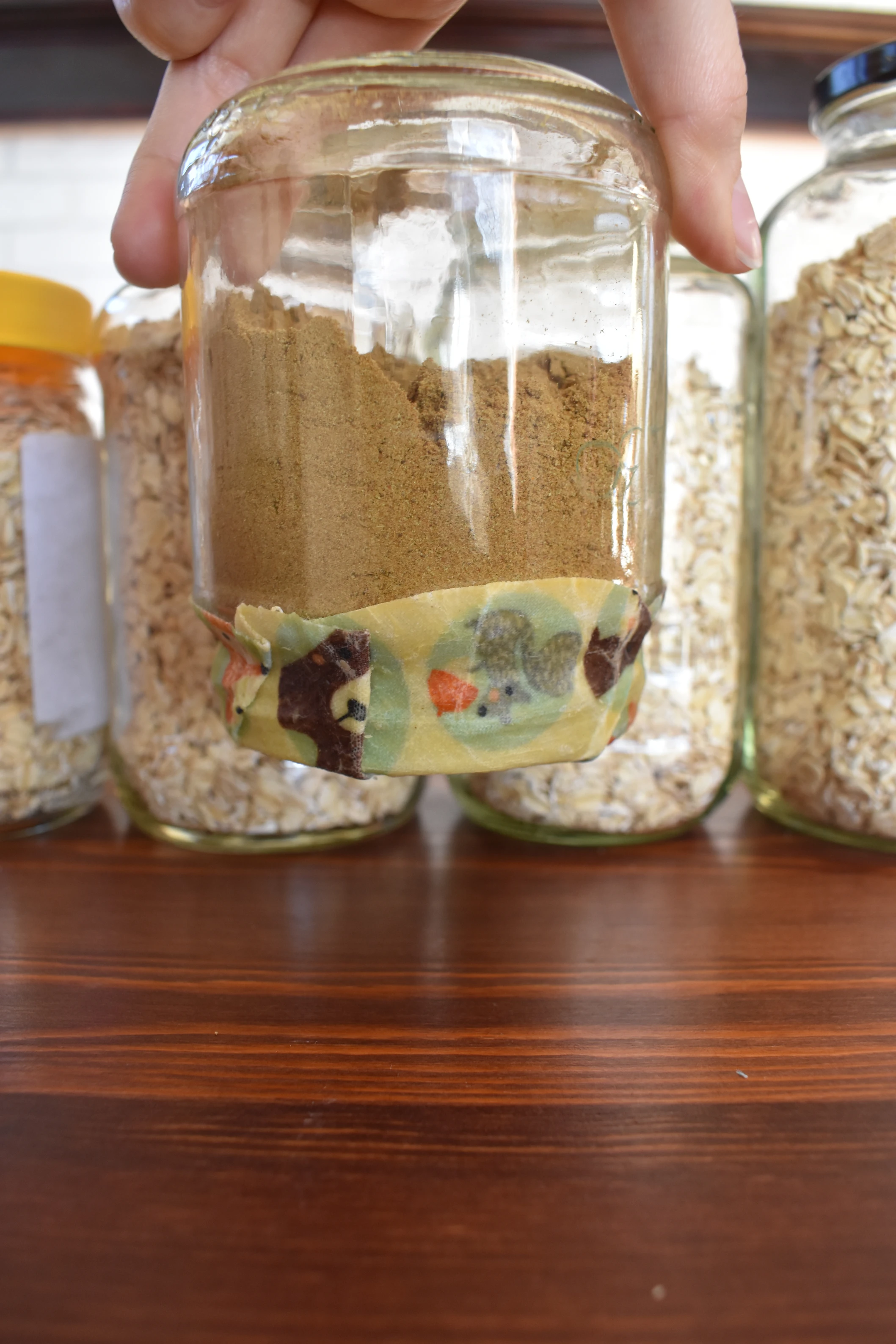 a glass jar is held upside down. inside the glass jar is cumin, a spice, and on the lid of the jar is a beeswax wrap.