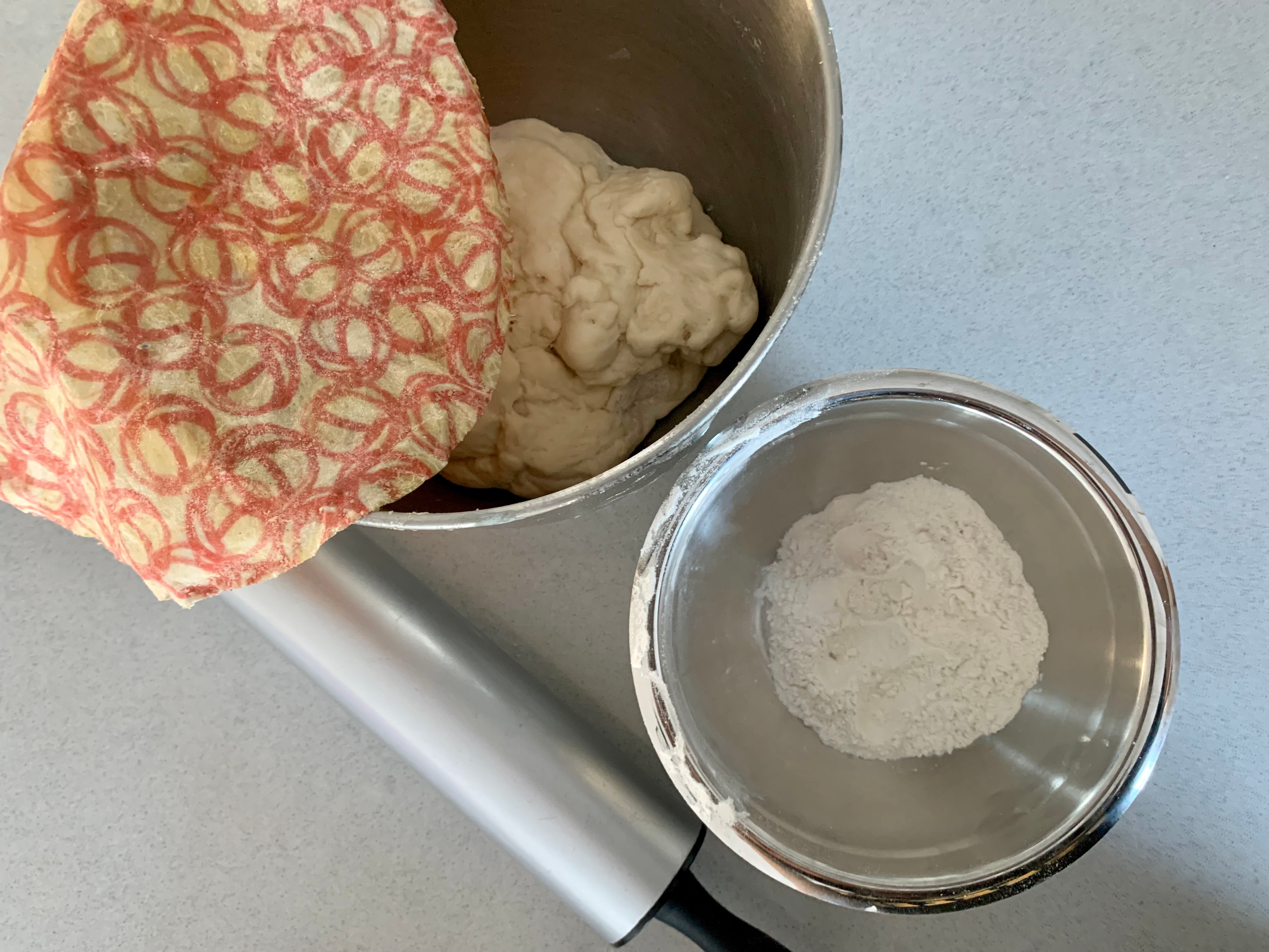 a white and pink beeswax wrap covers a bowl full of pizza dough so it can rise