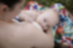 Infant looking over the shoulder of his mother as he breastfeeds in a field