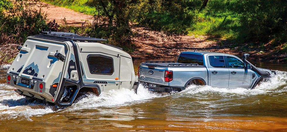 A pickup pulling the ARB Earth Camper through a small river.