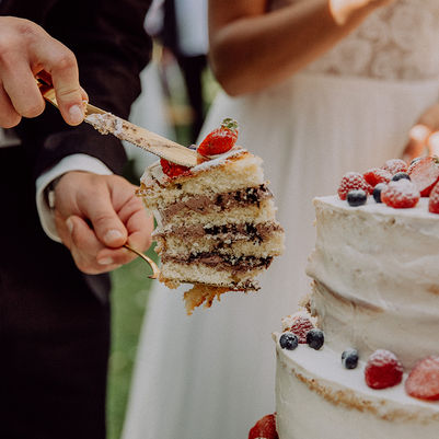 Stück einer Hochzeitstorte mit Schokoladenfüllung und Erbeeren oben drauf. Brautpaar schneidet Hochzeitstorte an