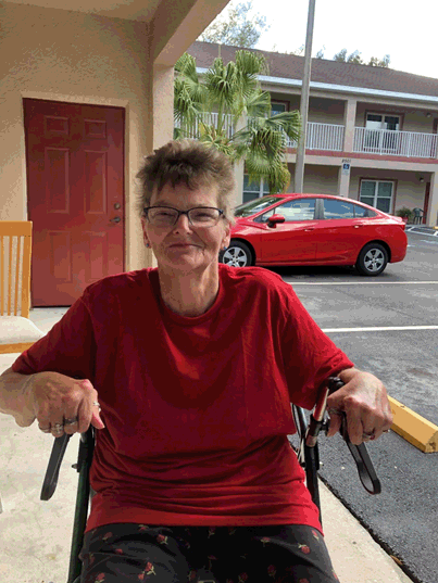 woman in a red shirt sitting in a wheelchair outside her apartment