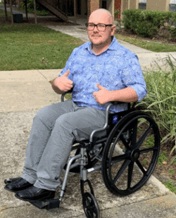 man in blue shirt in wheelchair giving the thumbs up signal