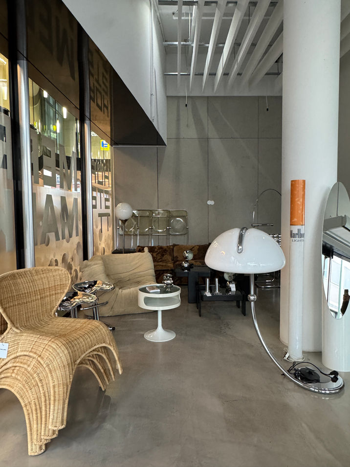 Cozy lounge area featuring rattan armchairs, a large chrome arc lamp, and vintage design furniture in the showroom.