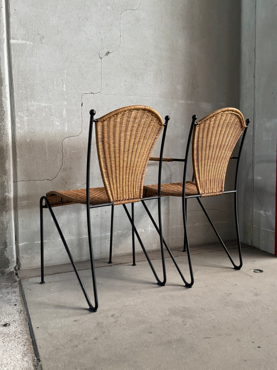 Rear angle view of two Frederic Weinberg wicker side chairs showing the black wrought iron frame