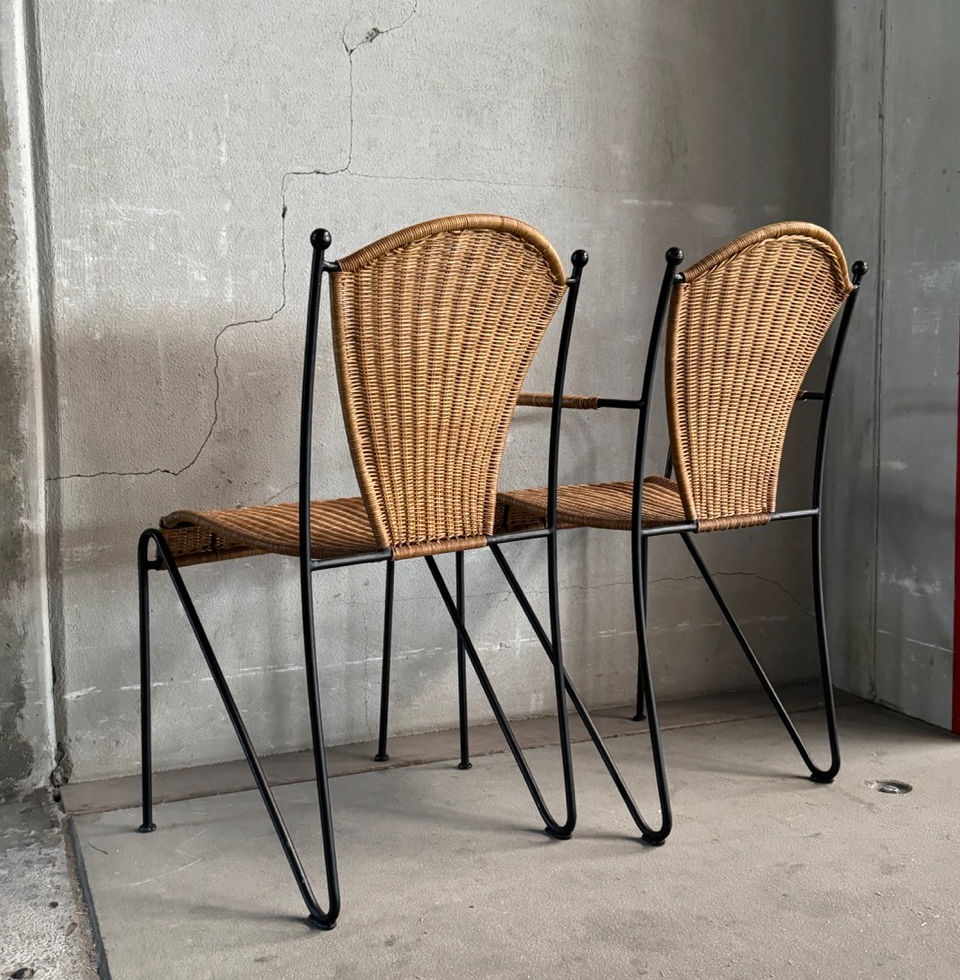 Rear angle view of two Frederic Weinberg wicker side chairs showing the black wrought iron frame
