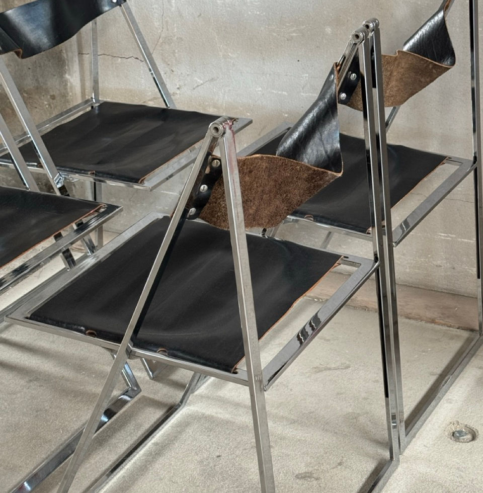 Close-up angled view of the minimalist chrome frame and black saddle leather seat
