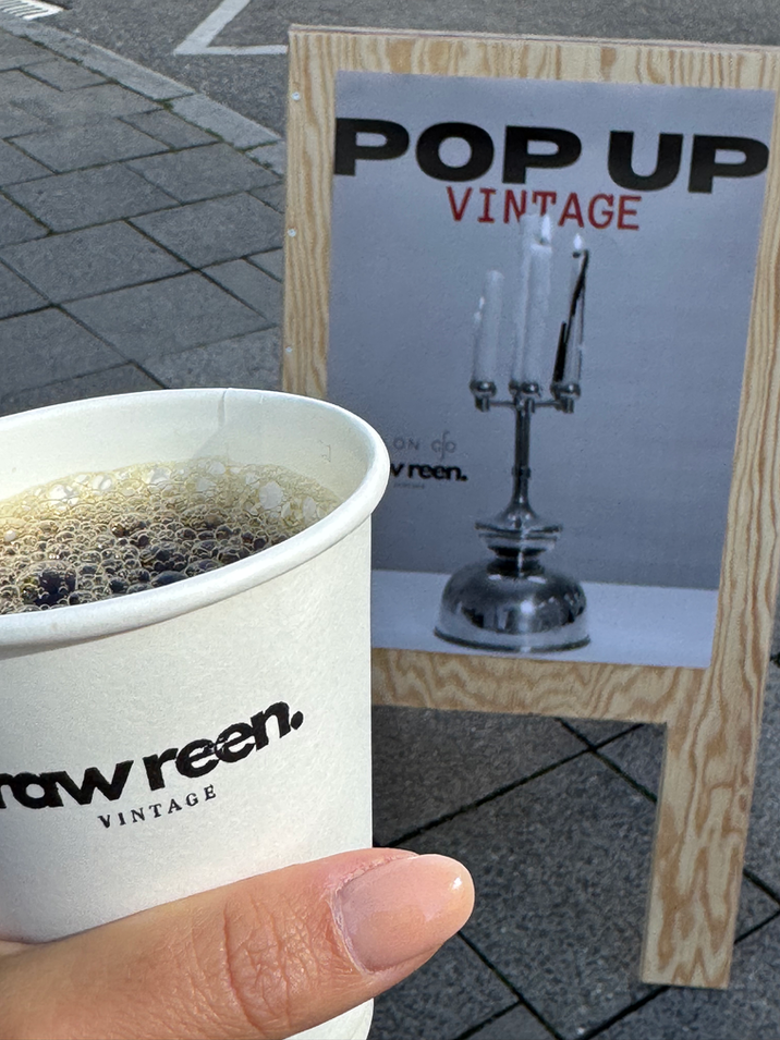 A Raw Reen Vintage coffee cup in front of the "Pop Up Vintage" welcome sign.
