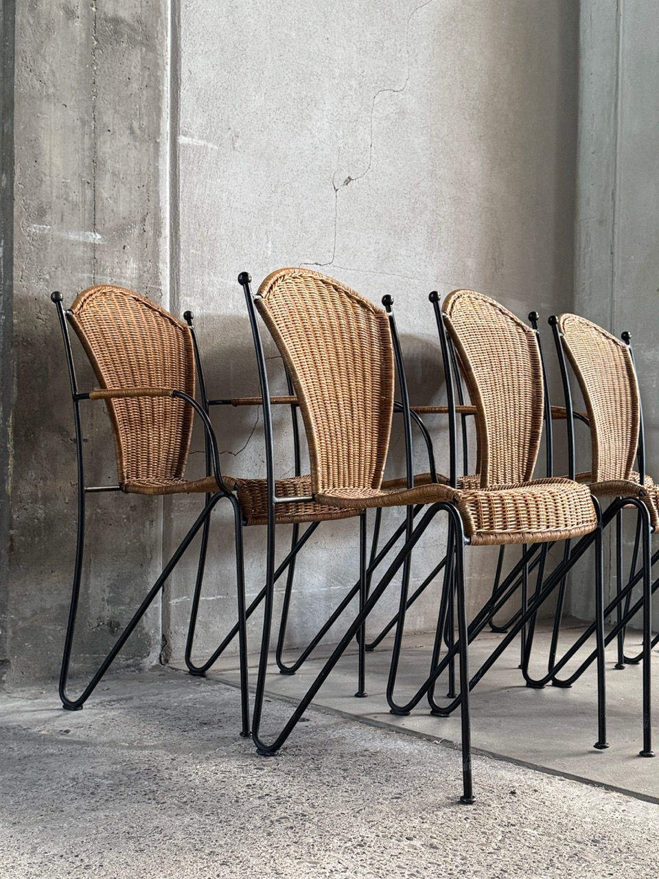 Set of 6 Frederic Weinberg wicker and iron dining chairs arranged in a minimalist concrete space