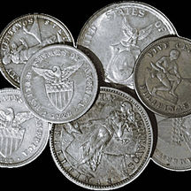 A group of United States–Philine (USPI) coins arranged together on a black background, featuring multiple denominations and designs from the American colonial period in the Philippines. Visible coins include centavos, a 1928 U.S.–Philippine coin with the American eagle and shield reverse, and a silver peso coin depicting Lady Liberty striking an anvil beside Mount Mayon. The image highlights the variety of Philippine coinage designs and denominations from the early 20th century.