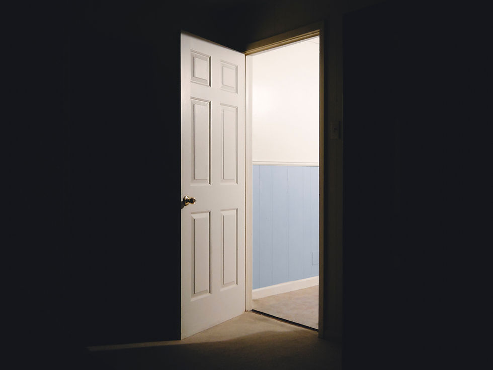 A door in a dark room opening to a light-filled hallway.