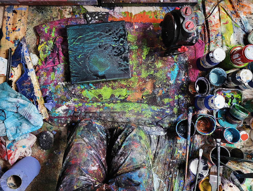 Overhead view of Emma Kinlough’s painting workspace, with mixed paints, brushes, and tools arranged across a textured surface