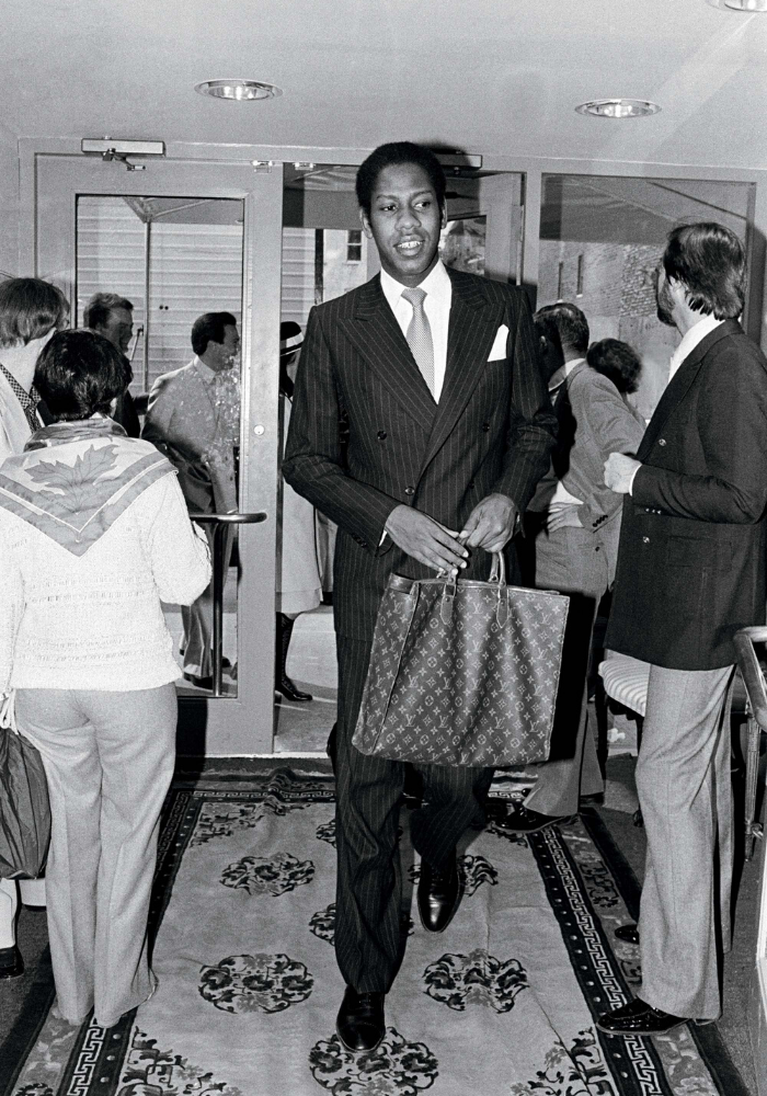 Andre Leon Talley Walking carrying a Louis Vuitton handbag