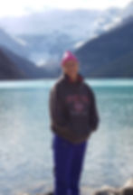 A photo of Bev with a lake and snow capped mountains behind her.