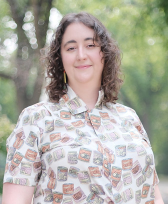 A smiling, standing person wearing a collared shirt outside.