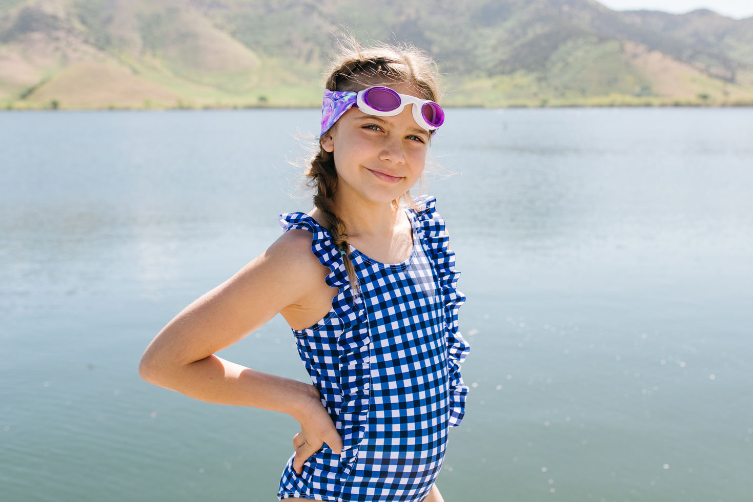 ילדה מחייכת עם משקפי שחייה, על רקע אגם