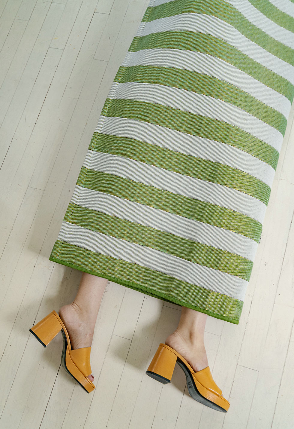 Green and white striped rug over feet in yellow heels.