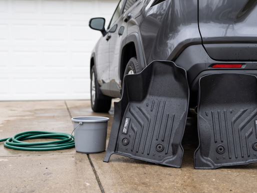Two freshly rinsed Maxpro floor liners drying against an SUV bumper on a driveway