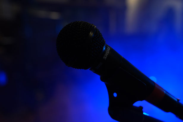 Silhouetted microphone against atmospheric blue stage lighting.