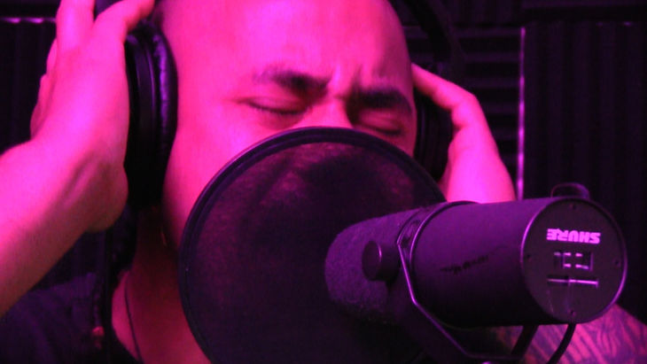 Vocalist wearing headphones and singing into a studio microphone.