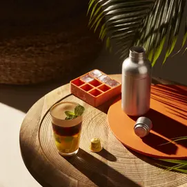 A table featuring a Nespresso coffee drink with ice cubes and an empty bottle beside it.