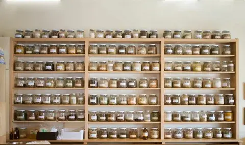 Shelves filled with labeled glass jars of herbs in an herbal shop.