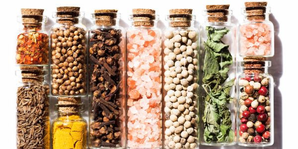 Glass jars filled with assorted herbs and spices including turmeric, cumin, peppercorns and dried leaves, symbolising the health benefits of everyday culinary herbs and spices.