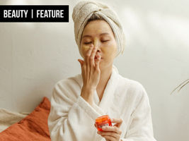 A Korean woman in a dressing gown applies cream to her face