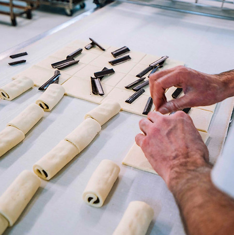 Geste du boulager viennois en train de garnir des pâtes feuilletées de bâtonnets de chocolat pour confectionner des pain au chocolat