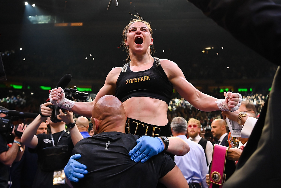 Boxer in black, arms raised triumphantly, is lifted by a supporter in a crowded arena. "GYMSHARK" visible on top. Jubilant atmosphere.