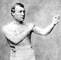 Man posing in a boxing stance, shirtless, in a vintage black-and-white photograph. Neutral expression, plain background.