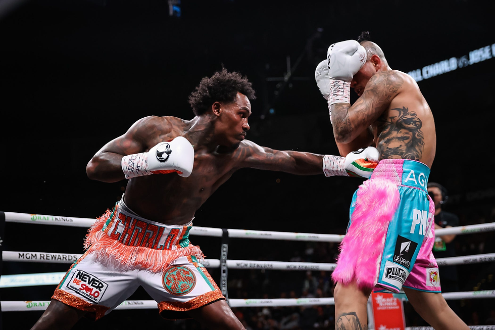 Boxer throws a punch at opponent shielding face. Bright shorts with "CHARLO" and pink fur detail, tattoo visible. Intense arena setting.