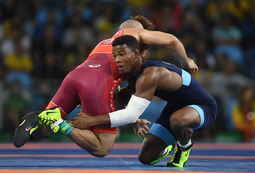 Two wrestlers in action on a mat; one in red, the other in blue and black, wearing neon green shoes. Intense focus and determination.