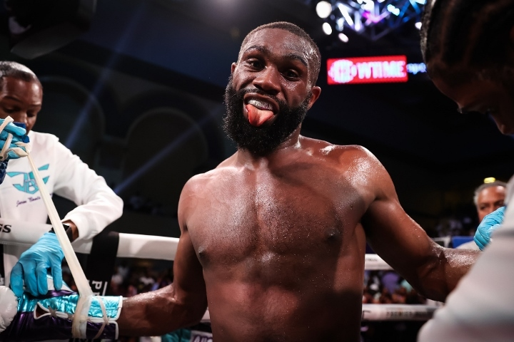 Boxer smiling with tongue out in a boxing ring, flanked by team members taping his gloves. Bright lighting, Showtime sign in background. Energetic mood.