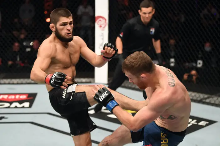 Two MMA fighters in a UFC octagon, one delivering a knee to the other. Intense focus. Black shorts. Referee in background.