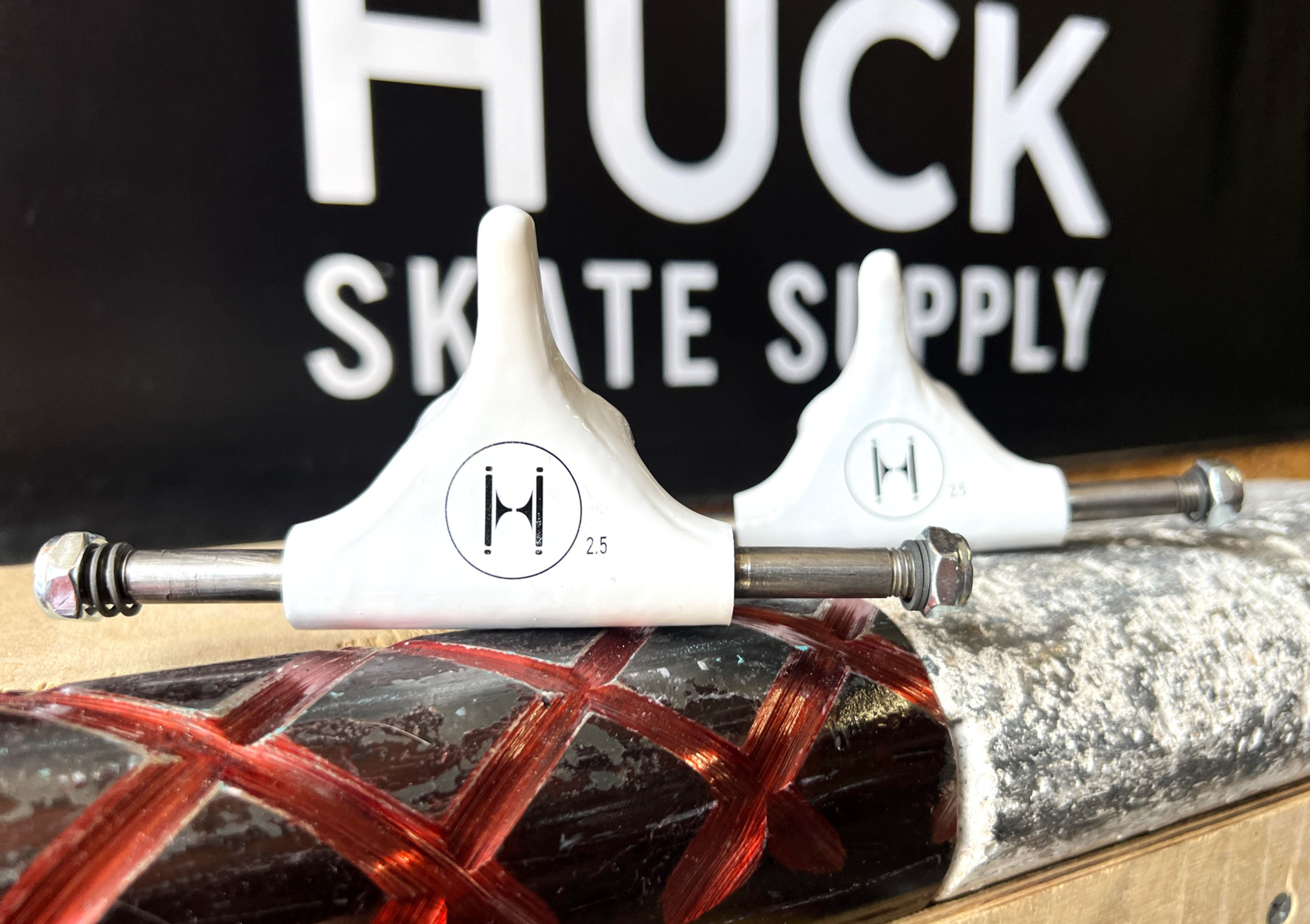 2.5" Huck trucks in white on top of skate coping, with a Huck Skate Supply banner in the background